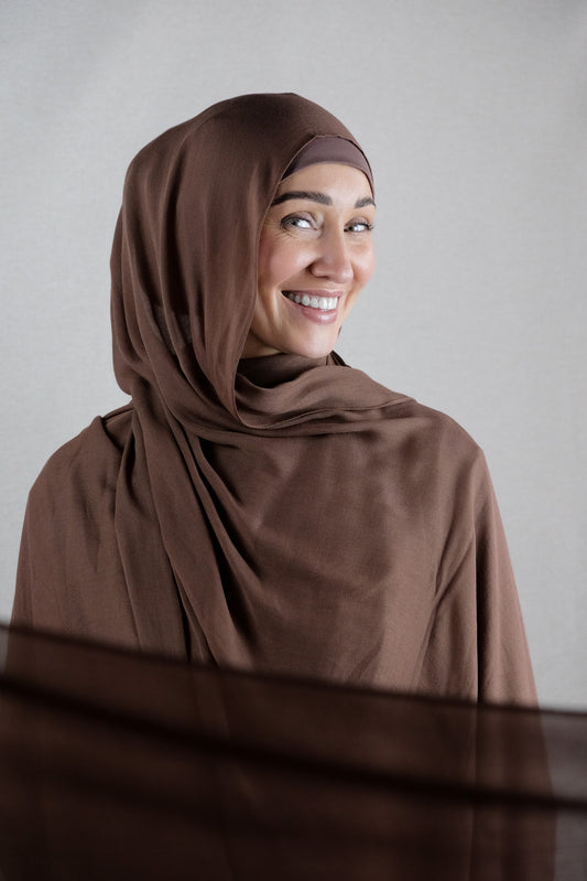 Woman wearing a brown hijab against a plain background